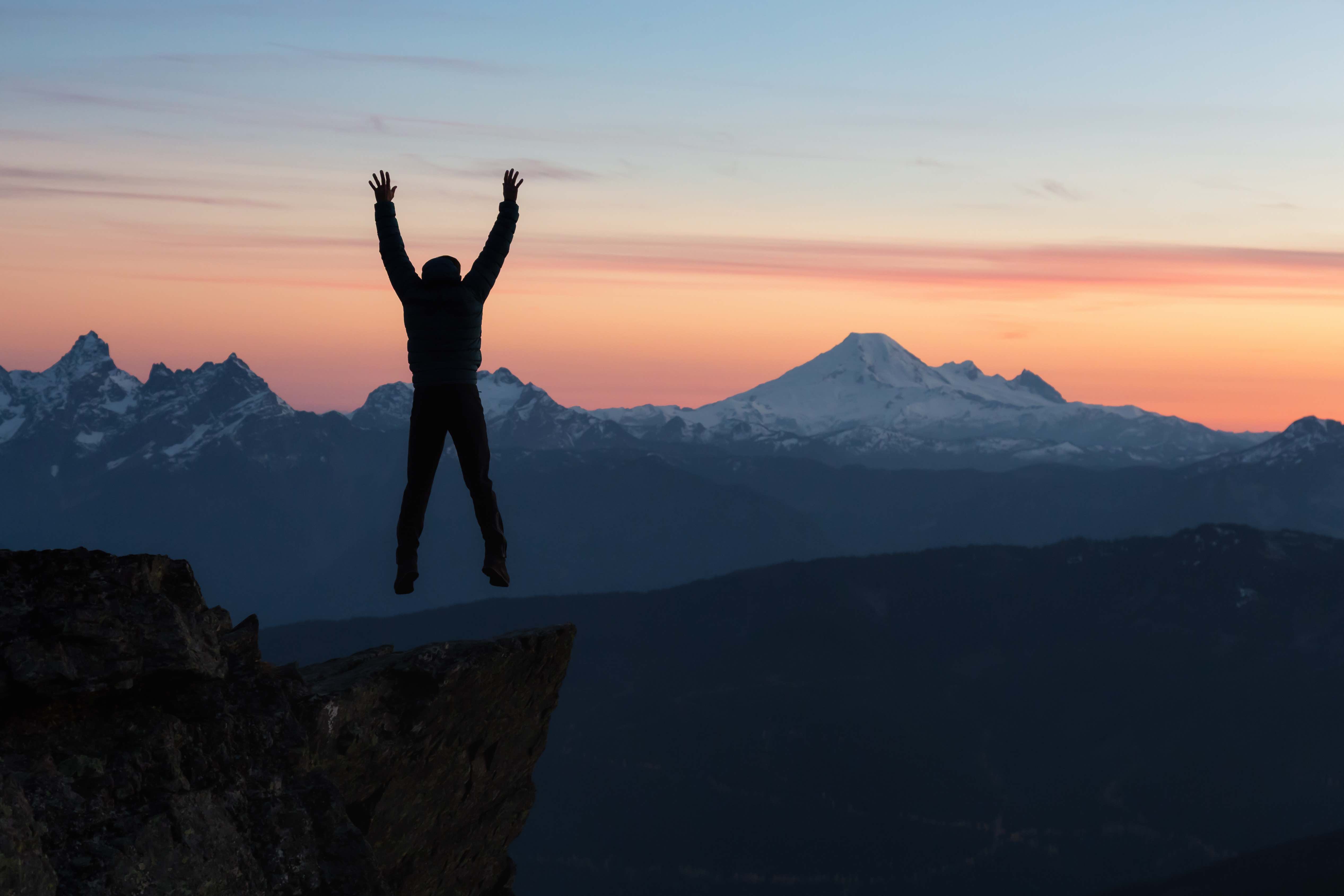 A man jumping into the air after climbing a high Wyoming mountain.