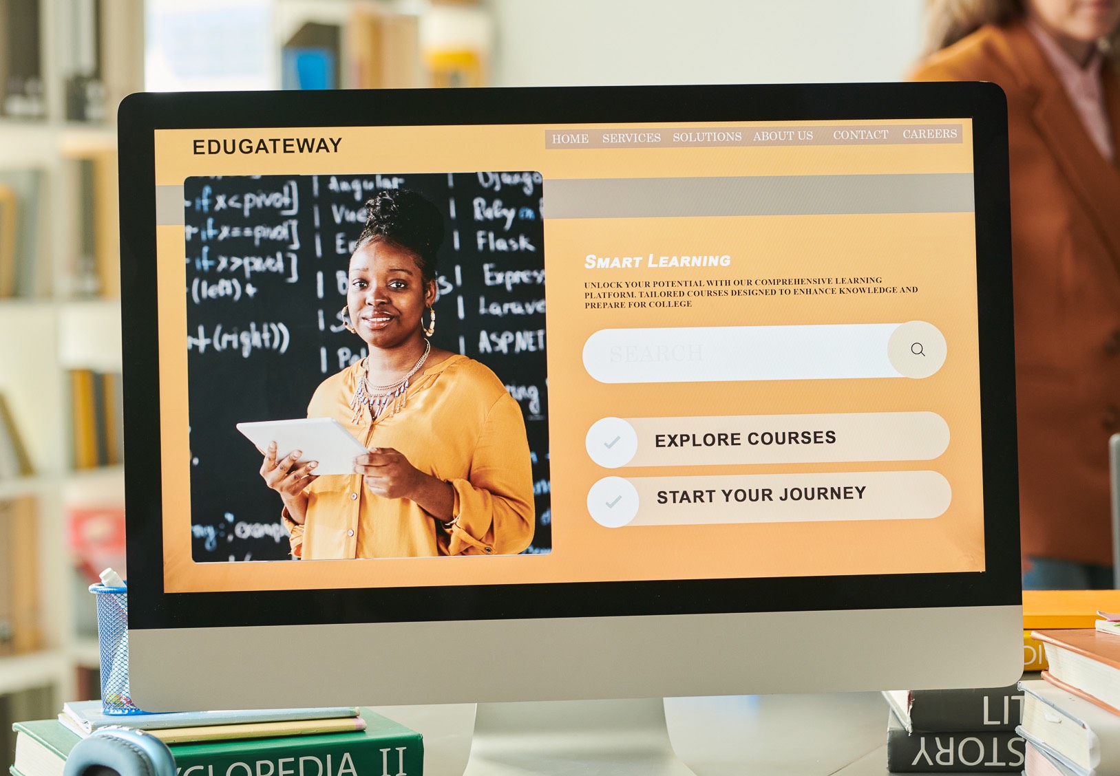 Photo of Computer with teacher running an online class with a messy desk full of books and other misc items.