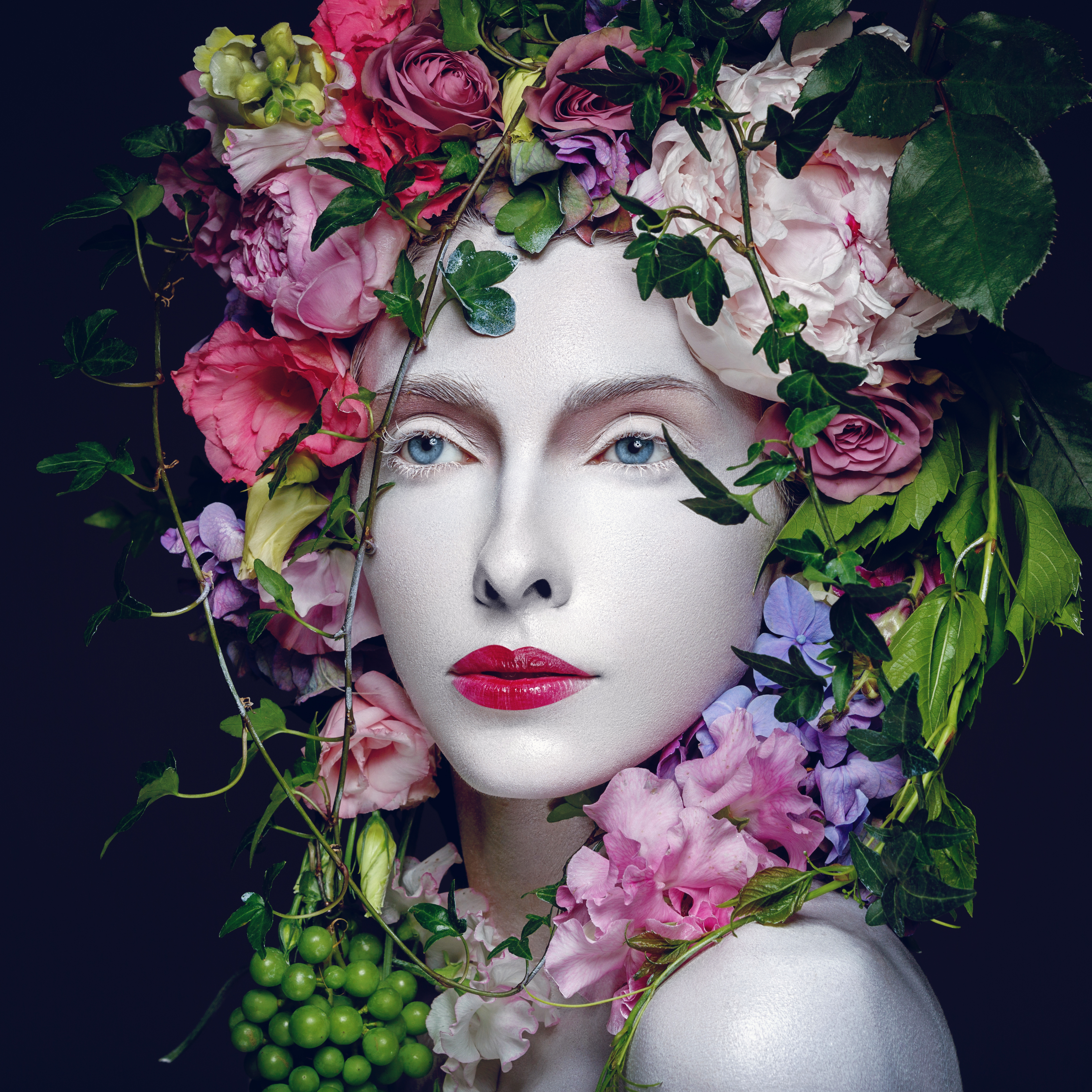 Beautiful, pale woman in red lipstick wearing a crown on flowers and grapes