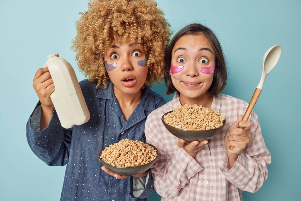 Mixed race women feel amazed pose with bowls of cornflakes big spoon and bottle of milk going to hav