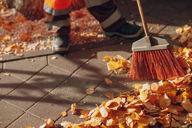 Janitor cleaner sweeping autumn leaves on the street.