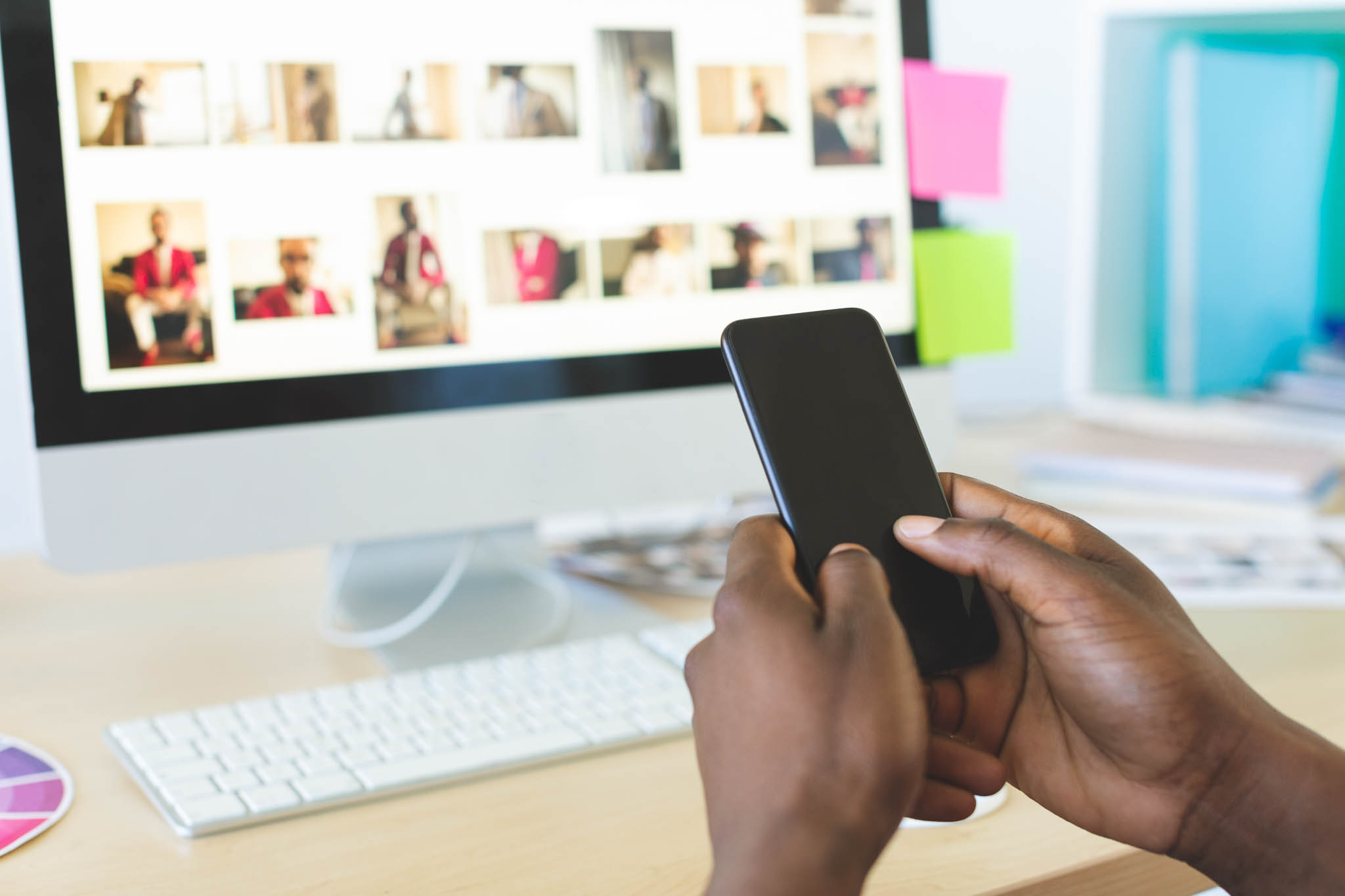 Person holding phone in front of desk in front of computer screen