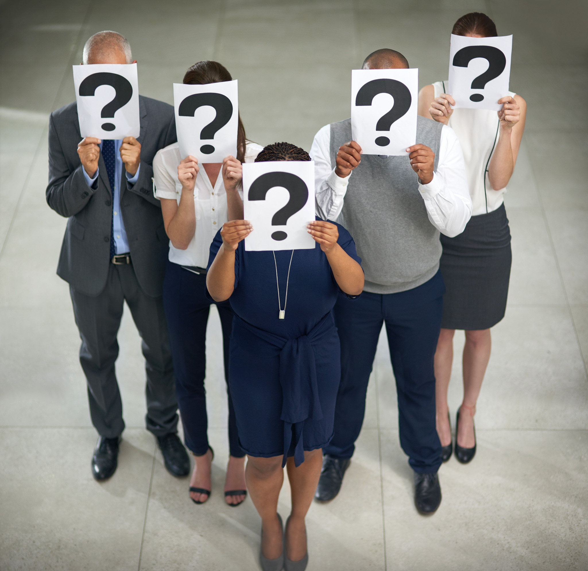 Photo of business professionals standing in a room with question marks on pages covering their faces