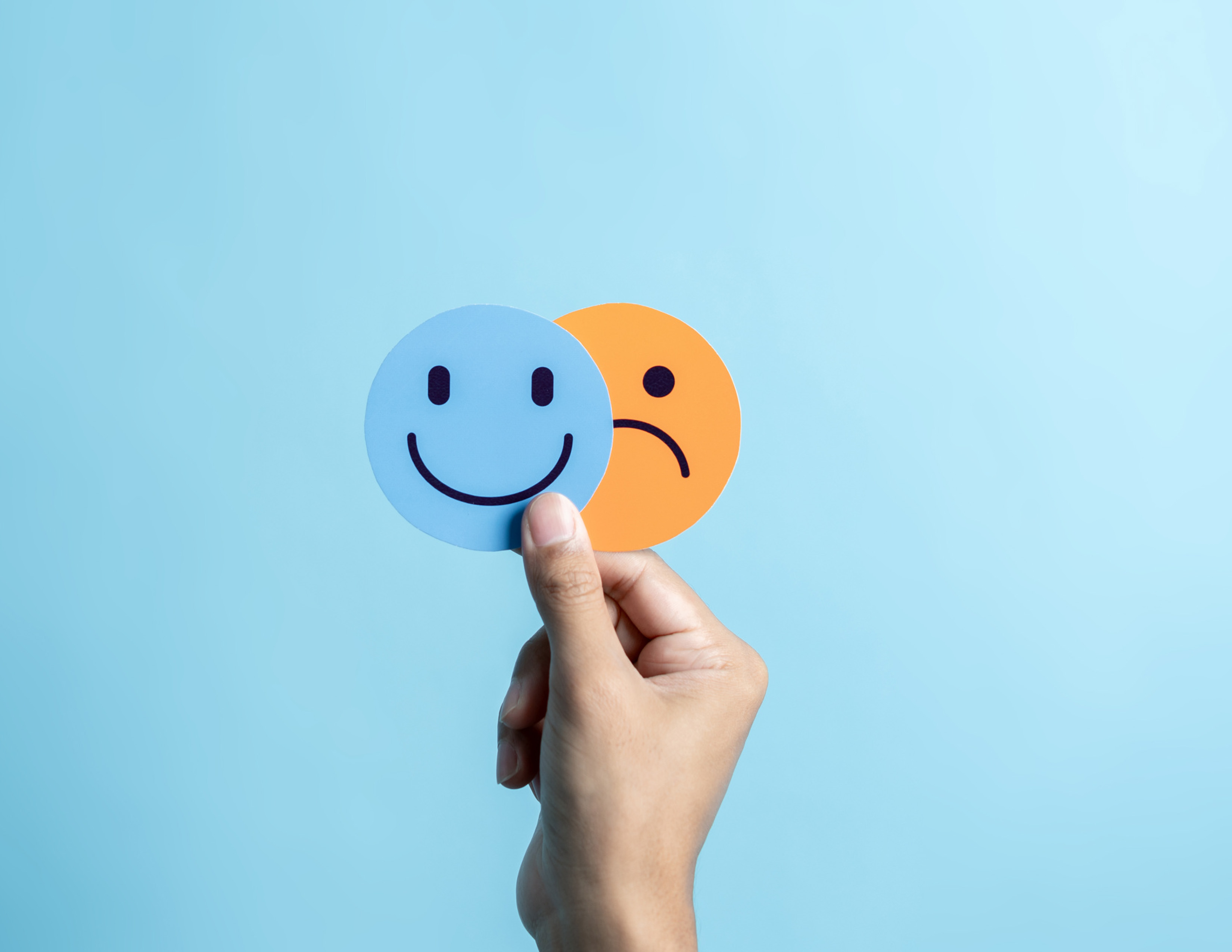 Image of hand holding smily and frowny faces in front of blue background