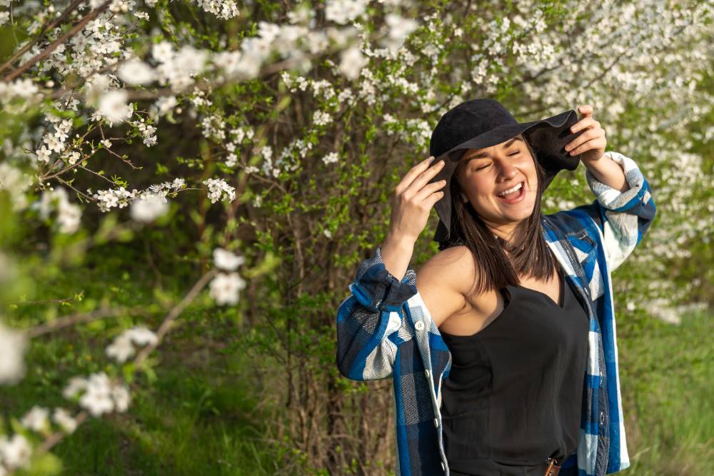 Attractive cheerful girl in a hat among the flowering trees in the spring, in a casual style.