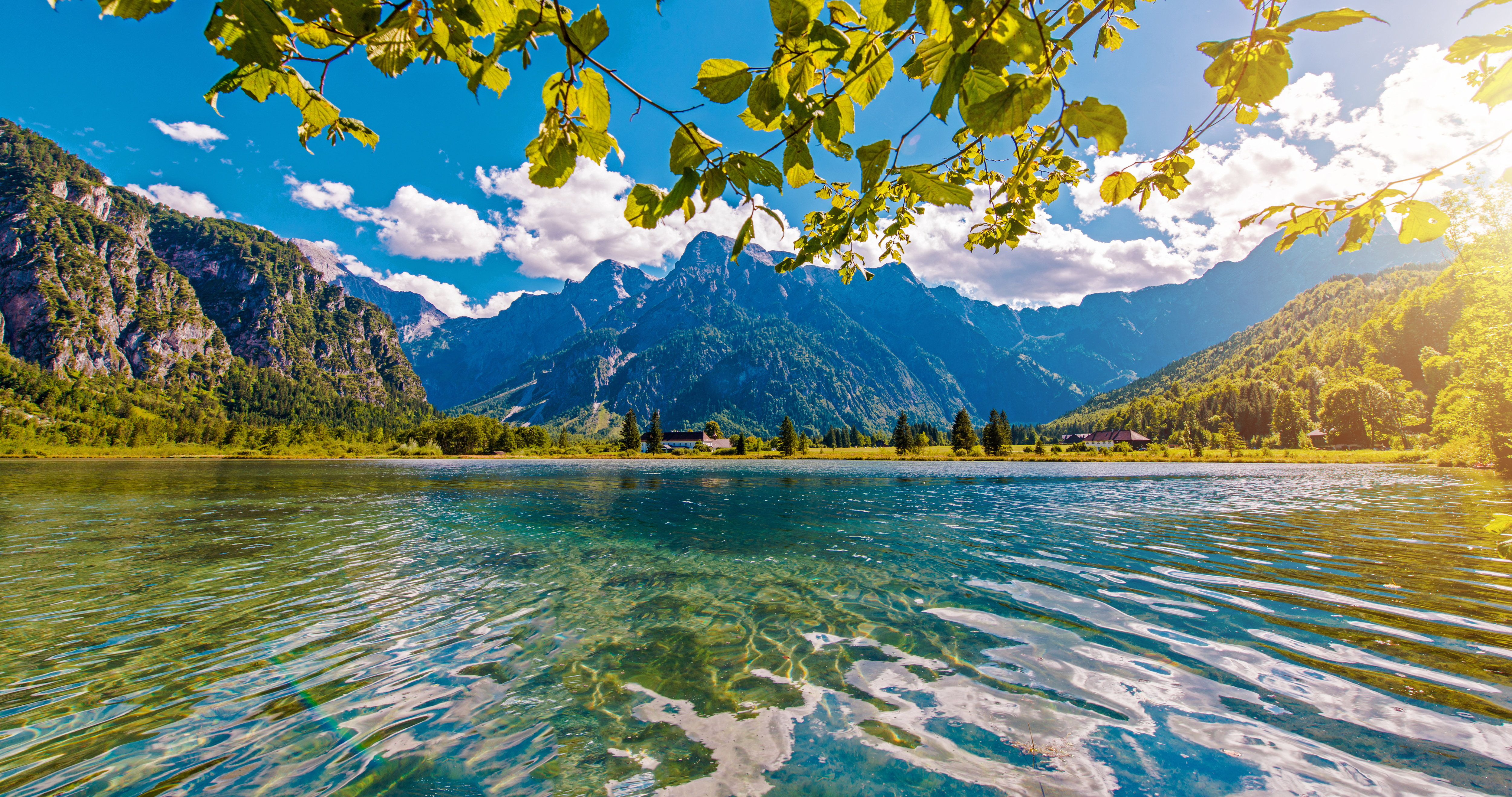 Image of shimmering mountain lake, dark green mountains in the background, framed by lush trees and cliffs